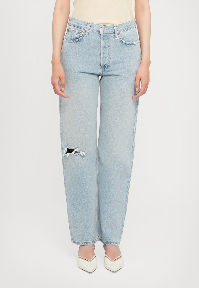 Light blue, high-waisted jeans with a relaxed fit, featuring a prominent ripped detail at the left knee. Cotton denim with a faded texture.