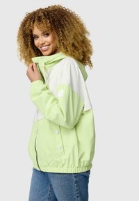 Veste zippée vert clair et blanche avec capuche, poignets élastiques et taille froncée. Texture lisse avec un design décontracté.