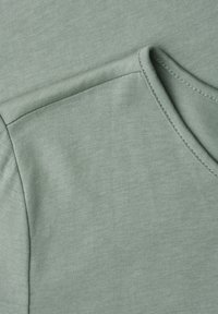 Gros plan sur un tissu vert doux montrant les coutures détaillées et les bords de couture d'un vêtement, probablement une chemise ou un haut.