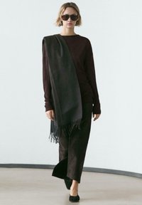 Długi bordowy top z długim rękawem w zestawie z pasującymi szerokimi spodniami. Na jednym ramieniu luźno opada ciemny szal z frędzlami. Czarne baleriny.