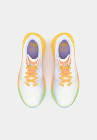 Chaussures de course avec une tige en mesh blanc léger, accents orange et jaune, semelle verte, et une semelle intérieure violette à motifs.