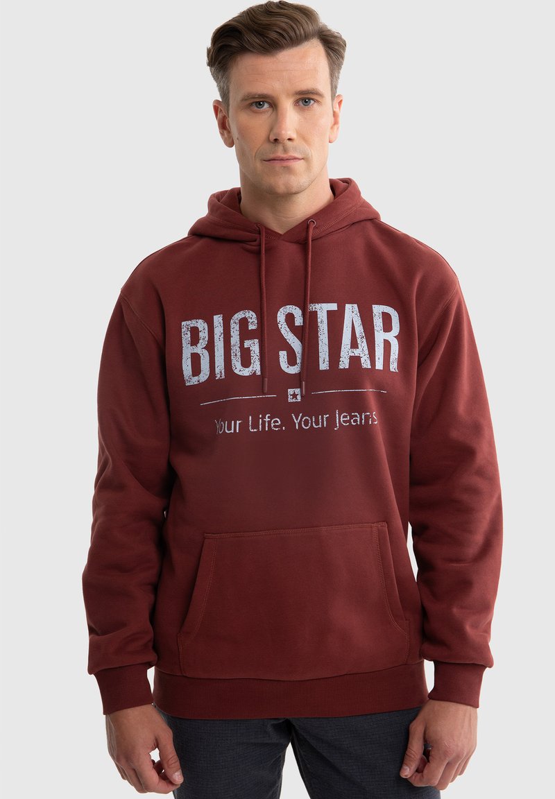 Bordeauxfarbener Kapuzenpullover aus weichem Stoff, mit einer Fronttasche und weißem Text: "BIG STAR" und "Dein Leben. Deine Jeans." auf der Brust.