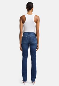 Jeans en denim bleu foncé avec une coupe droite, dotés de poches arrière fonctionnelles et de surpiqûres contrastées. Assortis à un débardeur blanc.