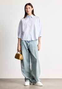 Ανοιχτό μπλε, υπερμεγέθη πουκάμισο με μανίκια τριών τετάρτων, σε συνδυασμό με ανοιχτό μπλε τζιν παντελόνι φαρδιάς γραμμής. Κρατώντας μια μικρή κίτρινη τσάντα χειρός.