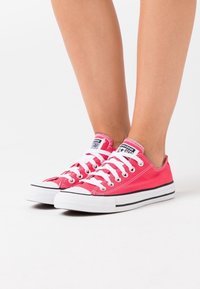 Punastest kangast sussidest valgete paelte ja kummitaldadega. Omab ümarat varvast ja musta triipu vahepealsel tald. Ikooniline bränding keelel.