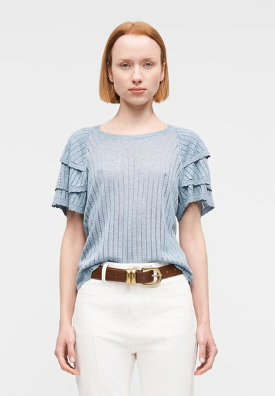 Haut en tricot bleu clair avec texture côtelée et manches évasées, associé à un pantalon beige et une ceinture marron avec une boucle dorée.