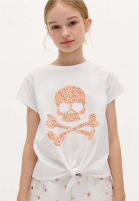 White t-shirt with short sleeves and a knotted front, featuring a colorful floral skull and crossbones graphic in pink, orange, and green.