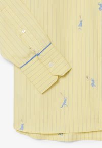 Camicia gialla con bottoni, a sottili righe verticali blu e piccoli motivi ricamati blu di giocatori di tennis su tutto il tessuto.