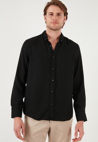 Camisa negra de manga larga con botones, hecha de un tejido texturizado, que presenta cuello y cierre de botones. Color liso y suave con un corte relajado.