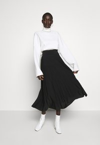 Black pleated midi skirt with a high waistband, paired with a white turtleneck sweater and white ankle boots. Smooth texture and flowing design.