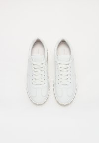 Białe sneakersy wykonane ze skóry, z niskim krojem, okrągłym noskiem, grubą gumową podeszwą z teksturowanymi akcentami oraz białymi sznurowadłami.