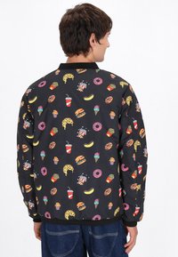 Giacca bomber nera con una stampa colorata a tema cibo, inclusi pizza, hamburger e gelato. Polsini ed orlo elastici.