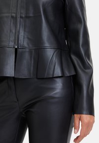 Černá kožená bunda s peplum lemem, se zipem v přední části a hladkou texturou, v kombinaci s černými koženými kalhotami s elegantním designem.