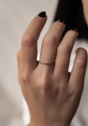 Anillo de oro con una superficie texturizada, ajustado de forma ceñida en un dedo, complementado por un esmalte de uñas negro en los dedos adyacentes.