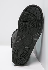 Semelle de botte en caoutchouc noir avec un motif de bande de roulement texturé, comportant un logo circulaire et des rainures pour l'adhérence, témoignant de la durabilité et de la stabilité.