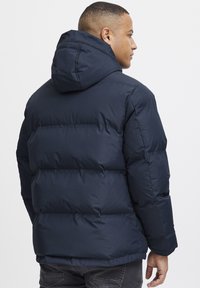 Jacket de puffer bleu marin cu glugă detașabilă, design matlasat și manșete elastice. Textură netedă și o croială lejeră.