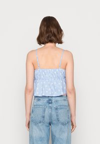 Top cortado, com estampado floral em azul claro, com alças finas, detalhes franzidos na zona do busto e uma bainha ampla. Combinado com jeans de cintura alta.