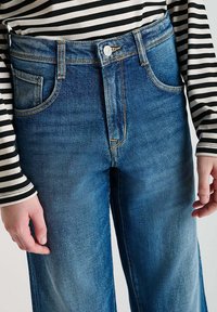 Jeans en denim bleu taille haute avec une coupe droite, dotés de poches avant, d'une fermeture à bouton et d'une légère décoloration pour apporter de la texture.