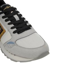 Sneaker grigia e bianca con lacci neri, punta in rete, sovrapposizioni in camoscio e una toppa con logo marrone sul lato.