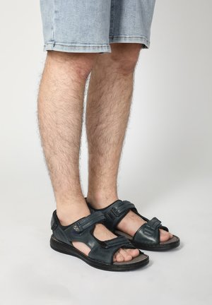 Mørkeblå lædersandaler med justerbare stropper og åben tå-design, båret med denimshorts. Har teksturerede detaljer og solide såler.