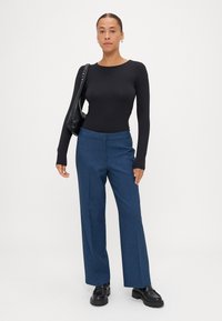 Zwarte lange mouwen bodysuit gecombineerd met blauwe op maat gemaakte broek. De broek heeft een subtiele textuur en een rechte pijp, aangevuld met zwarte schoenen.