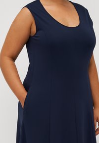 Marinblå ärmlös klänning med rundad halsringning, mjukt tyg och sidfickor, med en figurnära passform och subtila sömdetaljer.