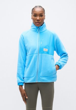 Jachetă din fleece albastru deschis cu guler înalt, fermoar frontal și un buzunar pe piept. Are un exterior texturat și manșete elastice.