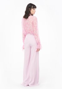 Blusa rosa trasparente con stampa leopardata e maniche a volant, abbinata a pantaloni a vita alta e gamba larga di un rosa chiaro.