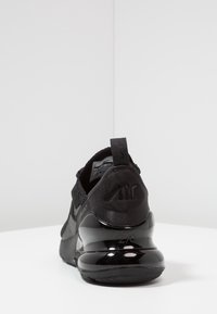 Botte de sport noire avec un dessus en mesh et un talon brillant. Comprend une languette de traction et des accents texturés, étiquetée "Air" à l'arrière.