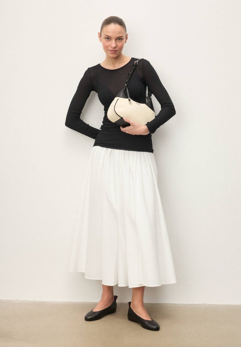 Haut noir à manches longues, jupe fluide blanche, ballerines noires et sac à main crème avec une sangle noire. Textures lisses et détails de design minimalistes.