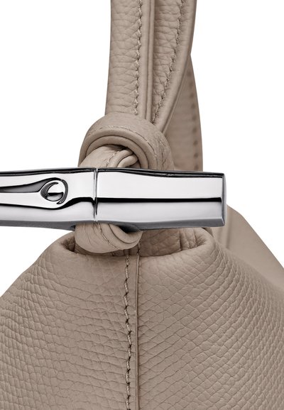 Beige leather handbag featuring a knotted handle, smooth metallic accent clasp, and textured surface with visible stitching details.