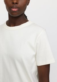 Cremefarbenes T-Shirt aus weichem Baumwollstoff, mit rundem Ausschnitt und kurzen Ärmeln, glatter Textur und minimalistischem Design.
