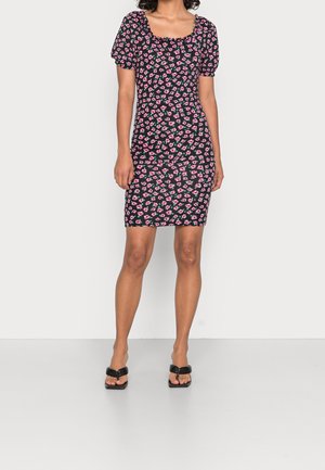 Robe noire à fleurs avec des motifs roses et verts, décolleté carré, manches bouffantes, design ajusté, longueur genou, associée à des tongs noires.