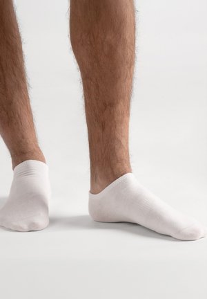 Weiße Knöchelsocken aus weichem Baumwollmaterial, mit geripptem Bündchen und figurbetontem Design, getragen auf einem nackten Fuß, teilweise sichtbare behaarte Beine.