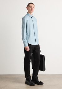Camisa de botones azul claro, pantalones negros, zapatos de cuero negros y un bolso tote negro. Textura suave y corte entallado. Diseño sencillo.