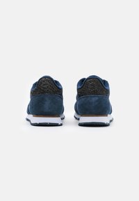 Baskets en daim bleu avec un talon noir texturé, une semelle blanche à accents mouchetés et un design athlétique classique.