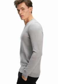 Pullover grigio a maniche lunghe con scollatura a V in una texture morbida. Presenta un design aderente e polsini a coste, indossato con pantaloni scuri.
