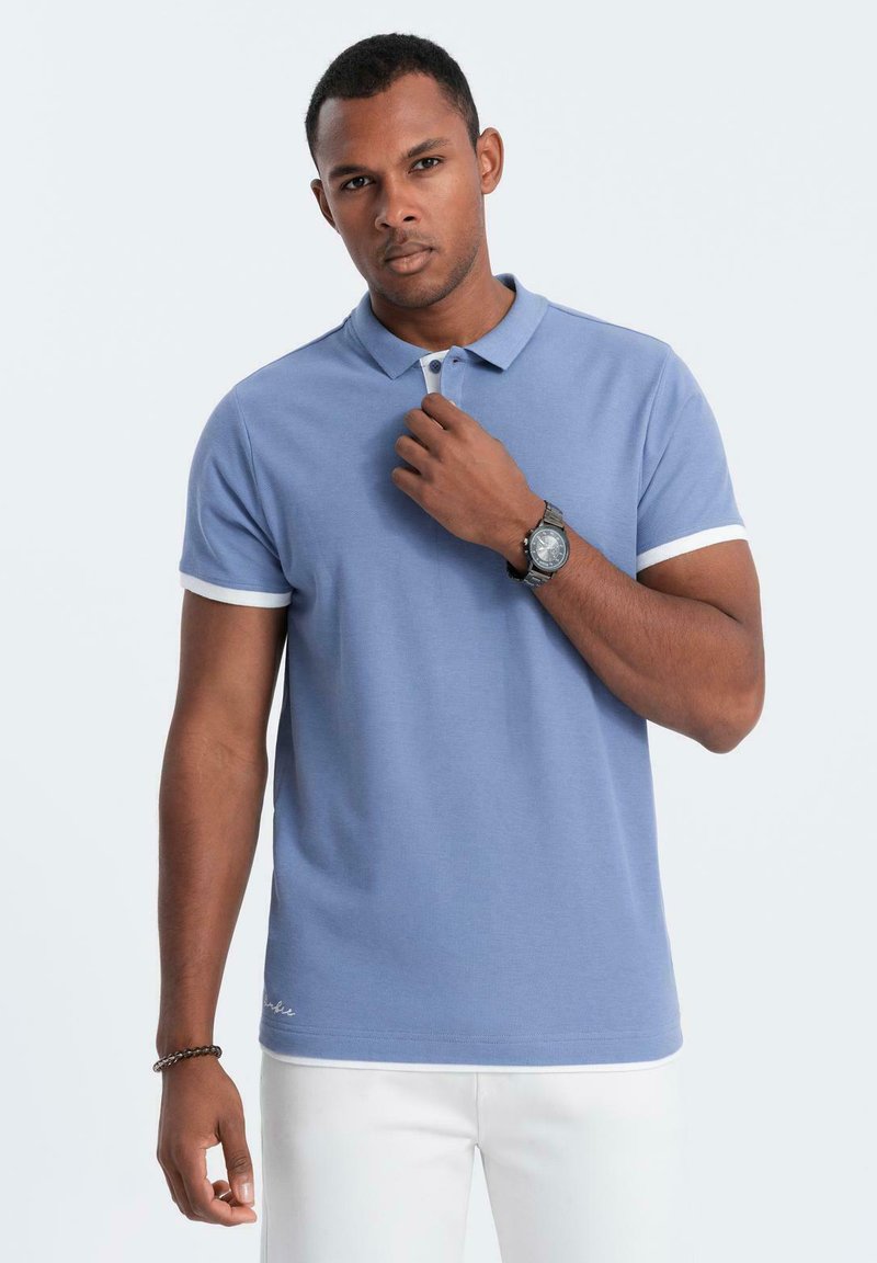 Světle modré polo tričko s krátkými rukávy a bílým lemem, které má knoflíkovou légu a vyšívaný detail blízko lemu.