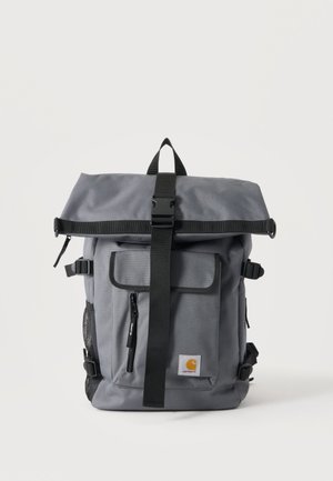 Gray Carhartt backpack with roll-top, black buckle strap, front zip pocket, side mesh pocket, and brand logo patch on front pocket.