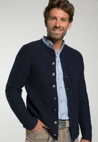 Marineblauwe gebreide cardigan met een textuurpatroon, ronde halslijn en zilveren knopen; gedragen over een lichtblauw overhemd met een gladde afwerking.