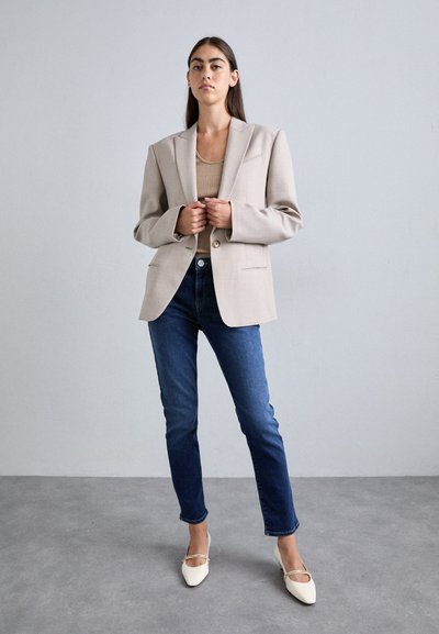 Μπεζ σακάκι, δομημένος σχεδιασμός, κλείσιμο με ένα κουμπί, συνδυασμένο με σκούρα μπλε τζιν και λευκά μυτερά παπούτσια. Απαλή ύφανση με ελάχιστες λεπτομέρειες.