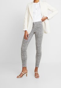 Pantalones ajustados de estampado de leopardo en gris y negro, con una textura suave, combinados con una blusa blanca y una chaqueta crema.