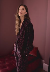 Sametist pidžaama komplekt sügavas burboonivärvis musta leopardimustriga. Sisaldab nööpidega särke ja nööriga pükse, millel on pehme tekstuur.