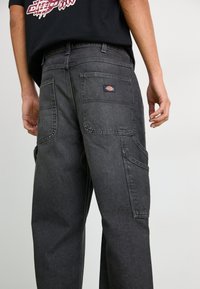Pantalons cargo gris foncé avec de multiples poches, des coutures contrastées et un petit patch logo à l'arrière. Silhouette à jambe droite.