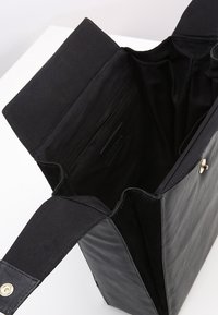 Svart tygväska med texturerad yta, öppen topp och en enkel rem. Insidan har en slät foder och sidoficka.