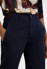 Temno modre hlače iz mehke tkanine s pravo obliko, z bočnimi žepi in zapiranjem na gumb v pasu.