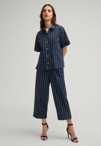 Camicia a maniche corte a righe blu navy con bottone frontale e taschino sul petto, abbinata a culotte ampie coordinate e tacchi neri con cinturini.