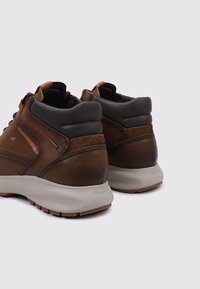 Bottines en cuir brun avec accents gris, col rembourré et extérieur texturé. Semelle en caoutchouc avec détails antidérapants. Conception imperméable.