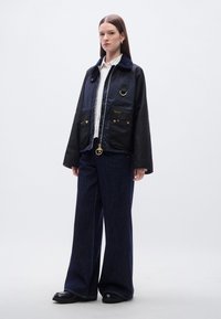 Μπλε ναυτικού και μαύρο μπουφάν με υφή, με χρυσά διακοσμητικά, γιακά, τσέπες και φερμουάρ. Συνδυασμένο με παντελόνι από σκούρο τζιν με φαρδύ μπατζάκι.