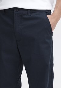 Granatowe chinosy z bawełny z płaskim przodem, bocznymi kieszeniami, szlufkami na pasek i pojedynczym zapięciem na guzik w pasie. Gładka faktura.